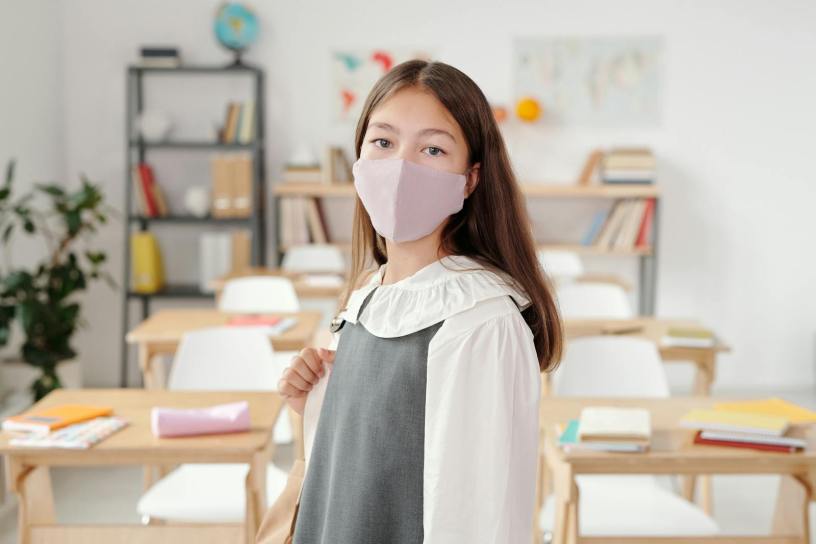 A schoolgirl in a classroom wearing a face mask, symbolizing new normal education.